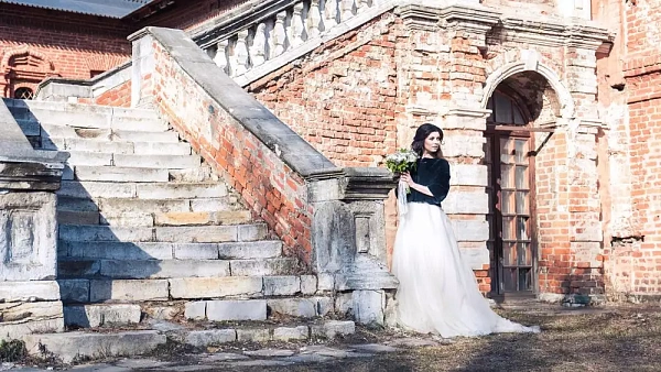 Свадебное платье с шубкой и длинным шлейфом на фоне старинного здания